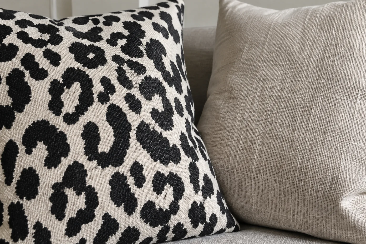 Détail d’un coussin animalier près d’une housse unie dont le grain du tissu est visible.