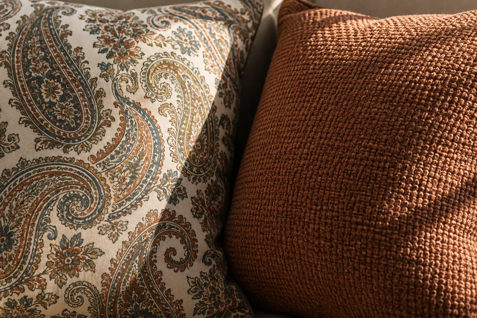 Détail d’un coussin cachemire lisse placé contre un coussin uni au relief textile visible.