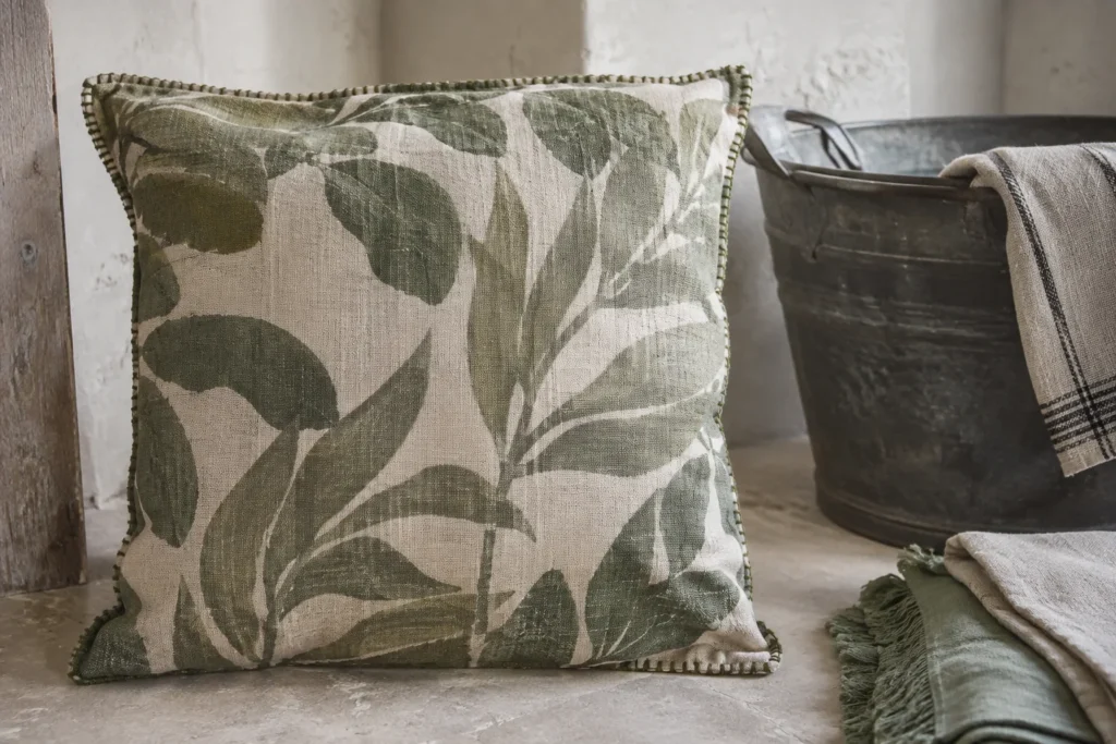 Housse de coussin à motifs et finition brodée posée près d’une bassine et de linge plié.
